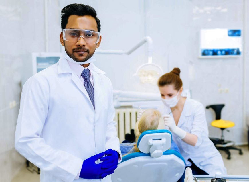 Portrait of a young confident asian male dentist in clinic in front of female dentist checking teeth to patient. Dental clinic concept